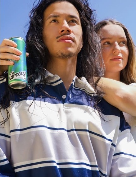 Two friends outdoors, one holding a green Groovy can