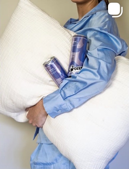 Person in pajamas holding a pillow and lavender Groovy Nightcap cans